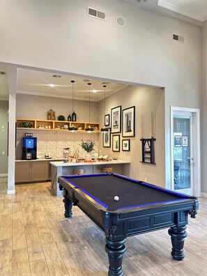 Une table de billard dans une pièce comprenant un coin cuisine, des meubles en bois et une machine à café.