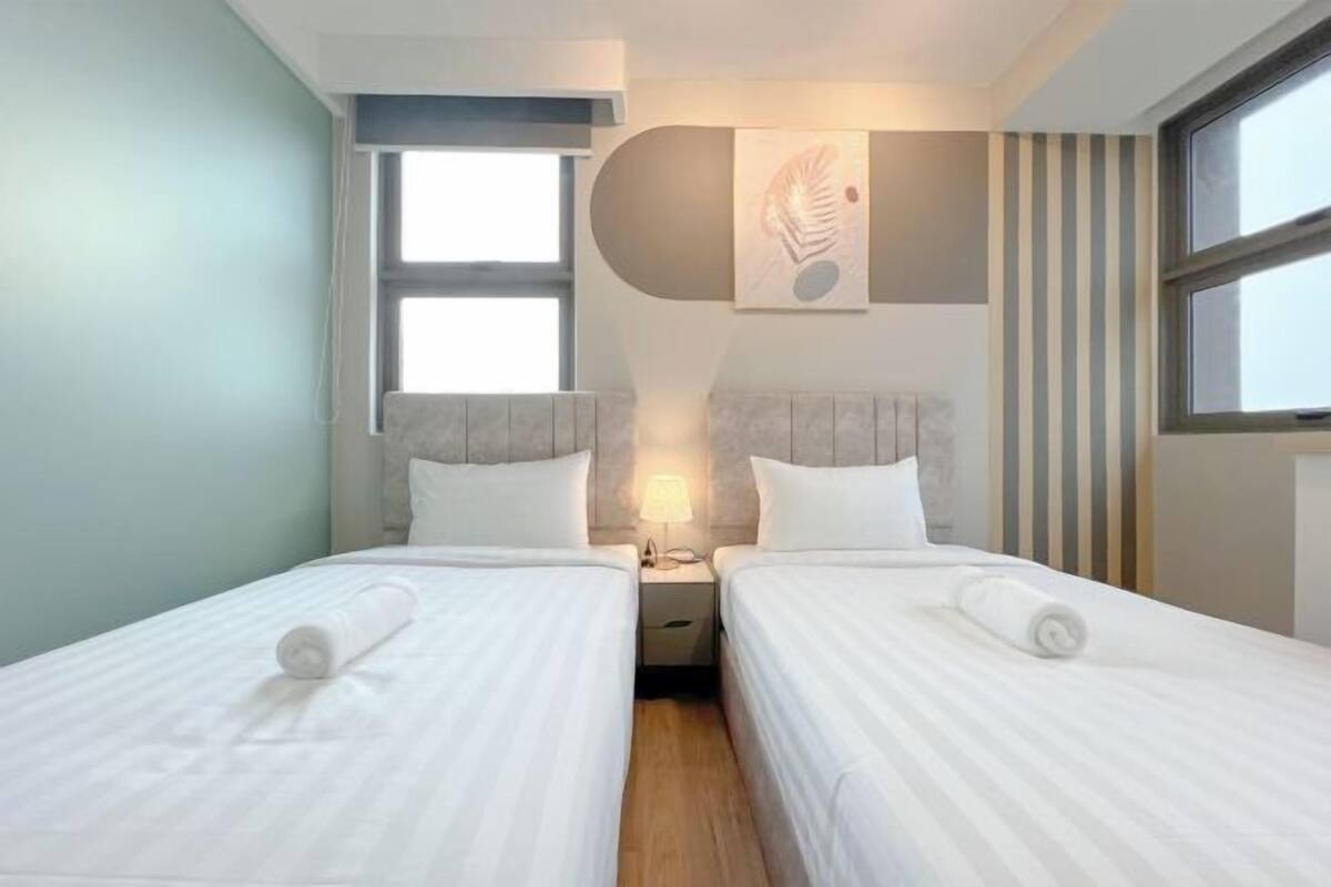 A hotel room with two beds, a nightstand, a lamp, and a large window.