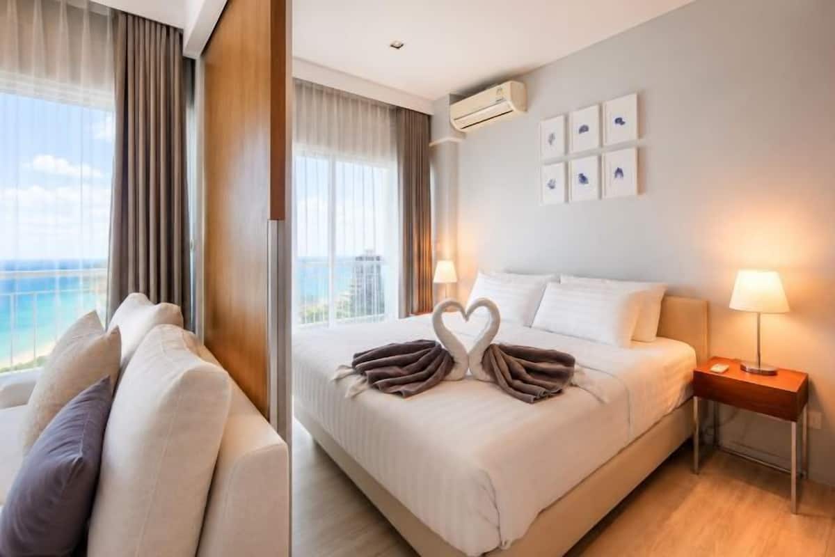 A hotel room with a bed, bedside lamps, a nightstand, and a view of the ocean.