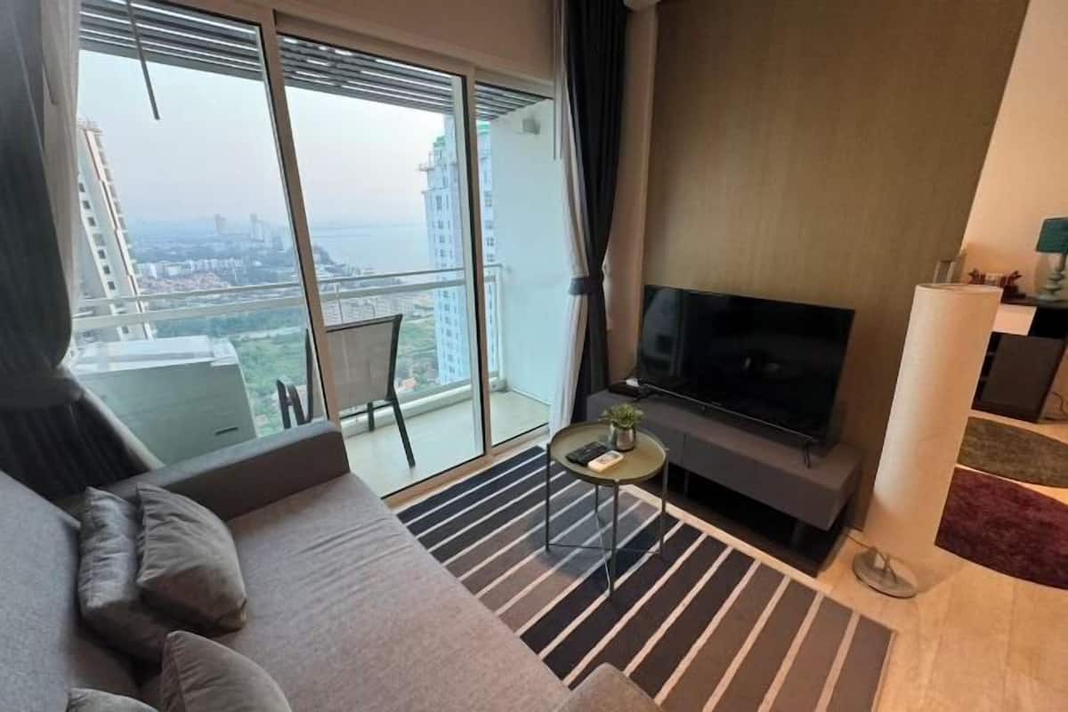 A modern living room with a sofa, TV, and a balcony with a view of the city.