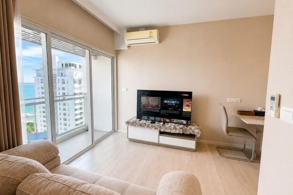 A modern living room with a flat-screen TV, a sofa, a dining area, and a view of the city.