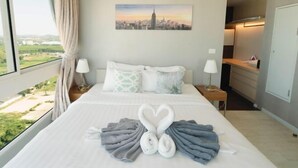 Quarto de hotel com uma cama, pintura de paisagem urbana, vista da cidade e toalhas dobradas em formato de coração.