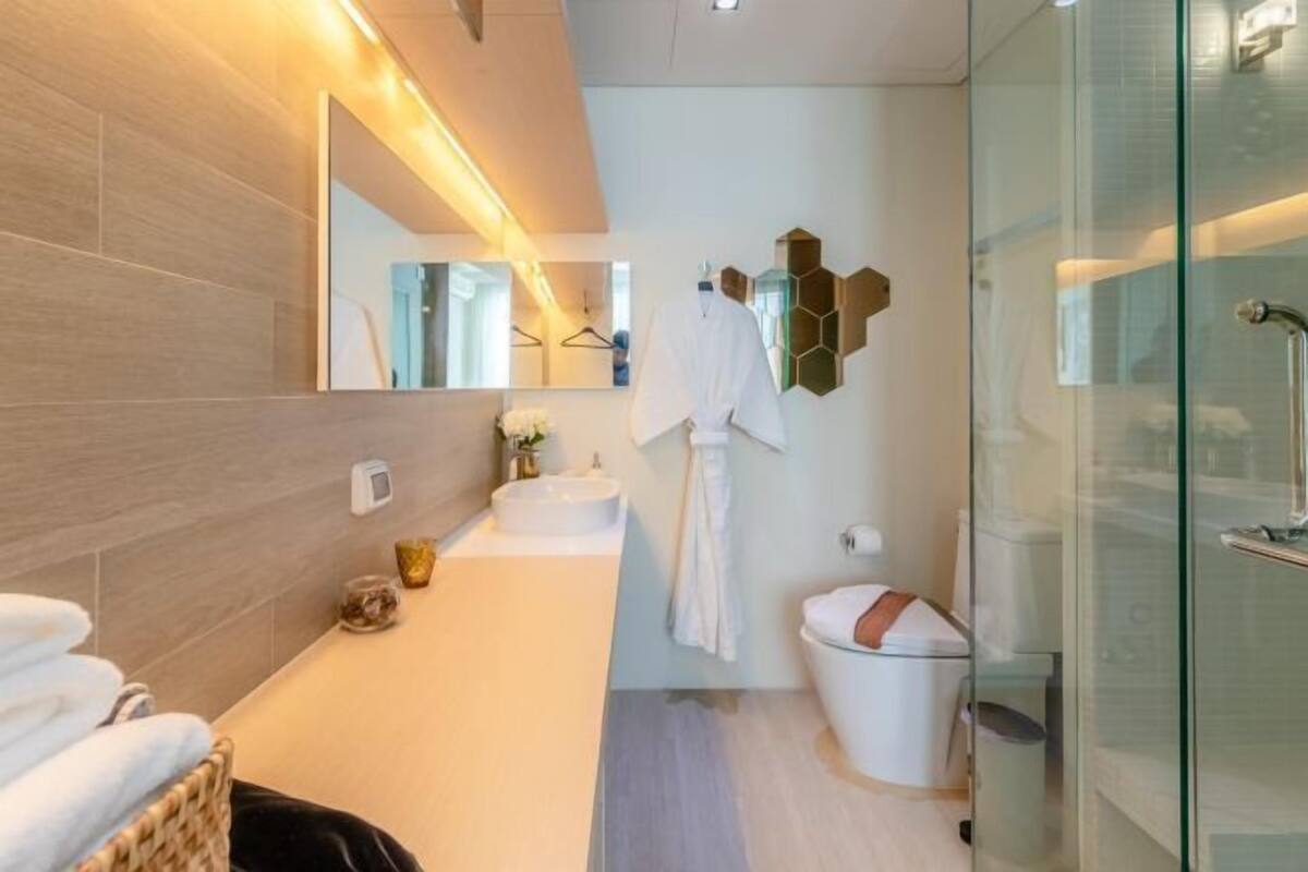 A modern bathroom with a large mirror, a round sink, a glass shower enclosure, and a white toilet.