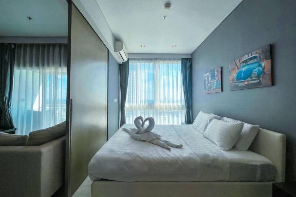 A hotel room with a bed, a sofa, and a large window with curtains.