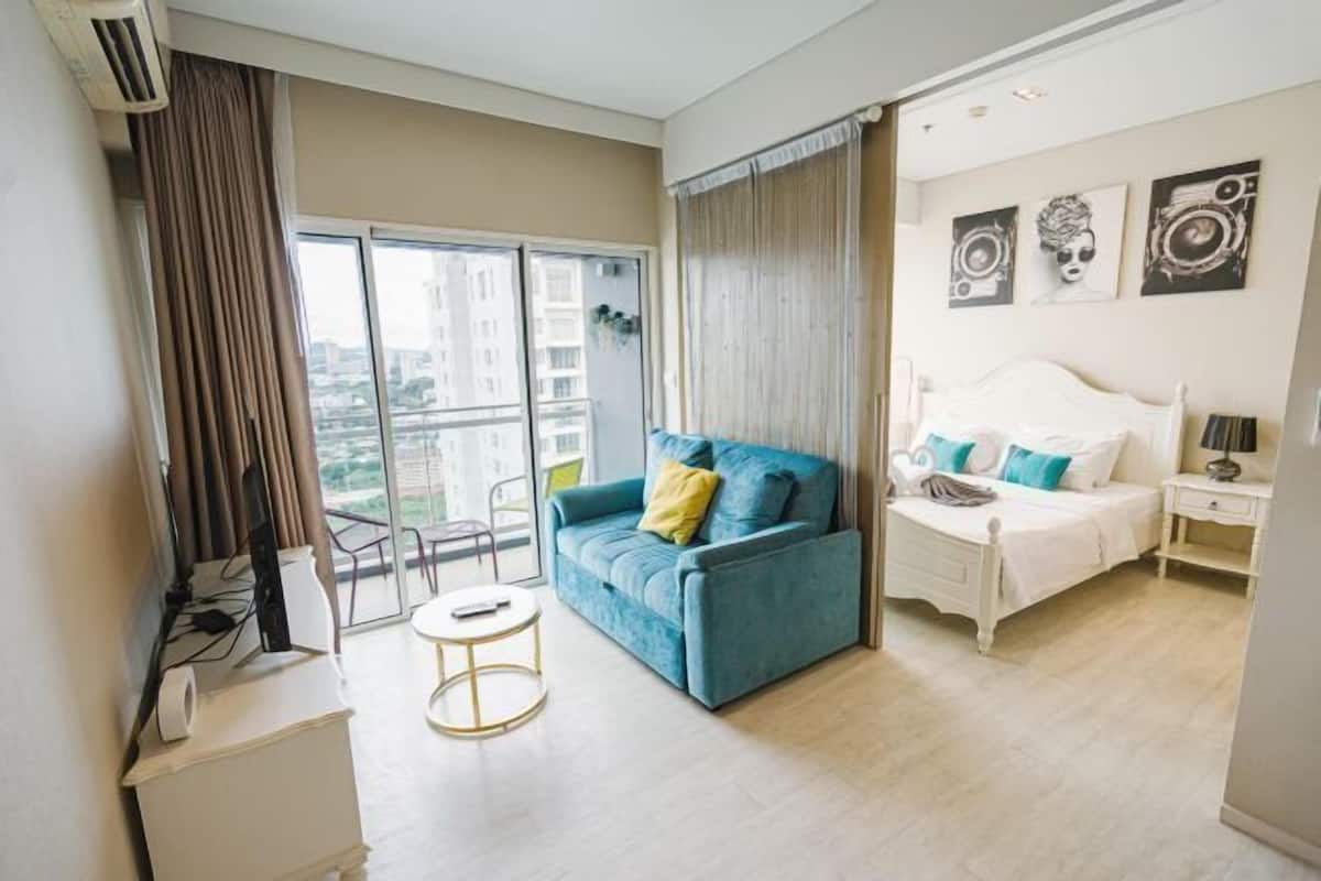 A modern hotel room with a large window, a blue sofa, a white bed, and a small round table.