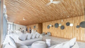 Uma área de estar espaçosa e moderna, com teto de madeira e um amplo espaço com sofás redondos e pufes acolchoados.