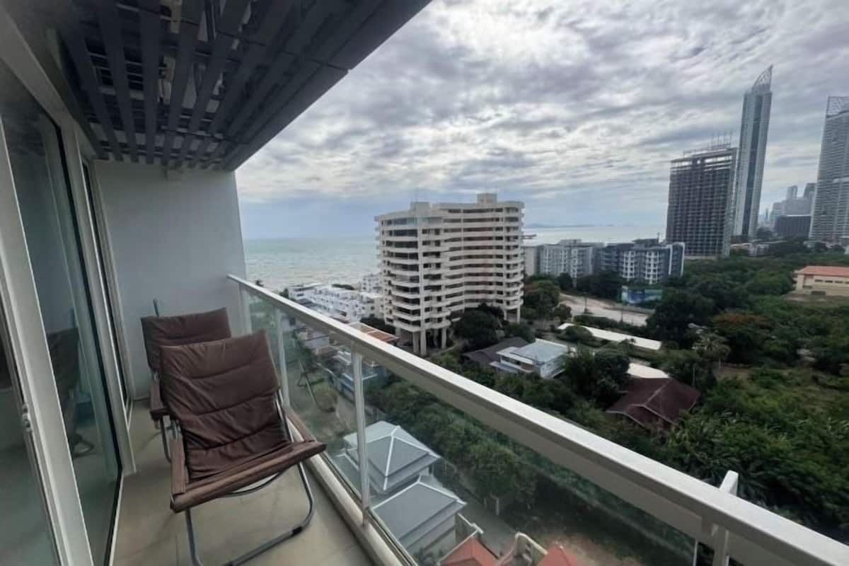 A balcony with a chair, a view of a cityscape, and a building under construction.
