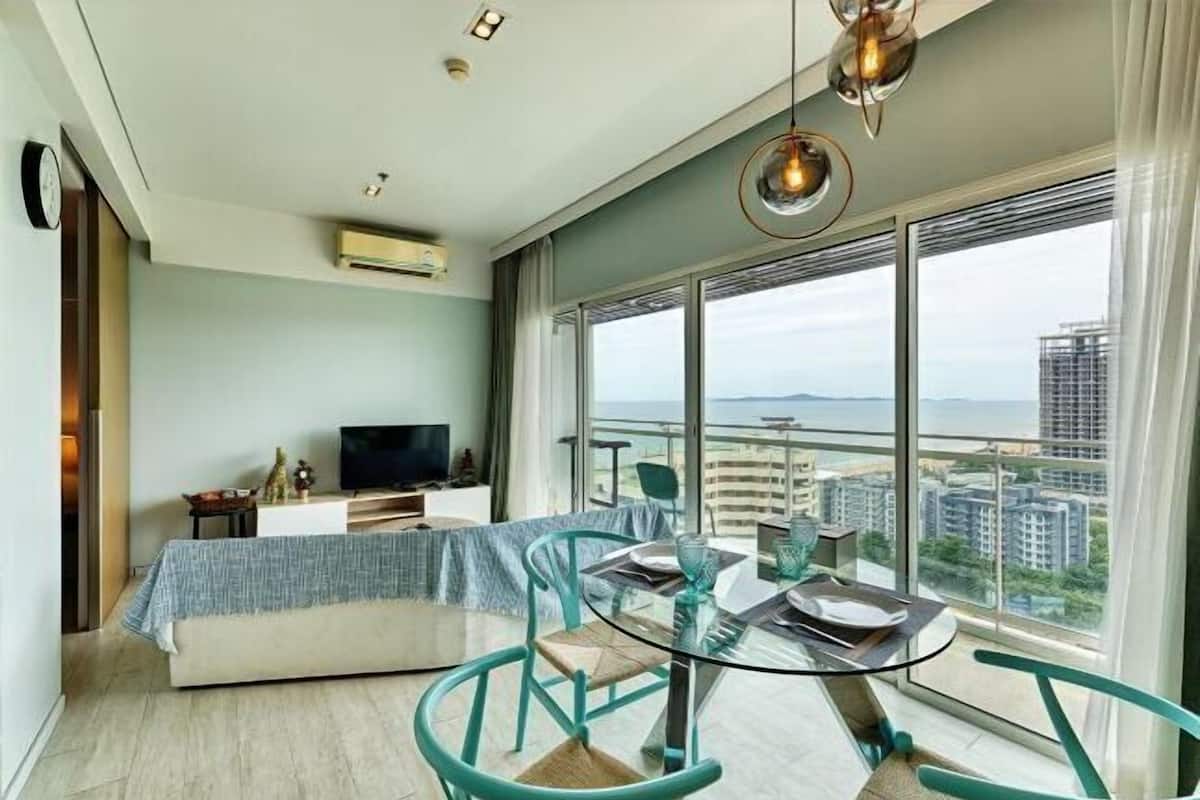 A modern living room with a glass dining table, teal chairs, a sofa, a TV, and a large window with a city view.