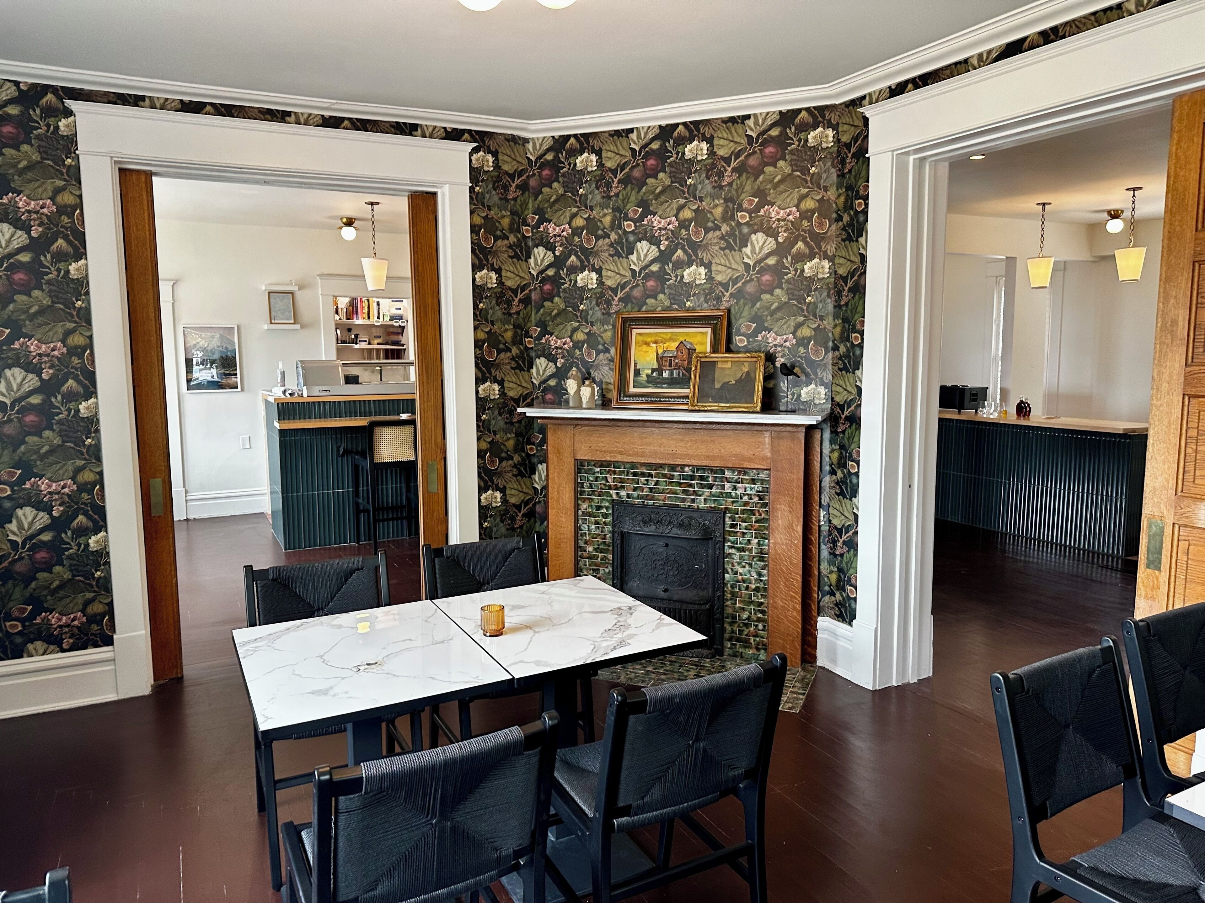 A dining area with a marble table and chairs, a fireplace with framed pictures, and a kitchen in the background.