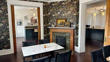 A dining area with a marble table and chairs, a fireplace with framed pictures, and a kitchen in the background.