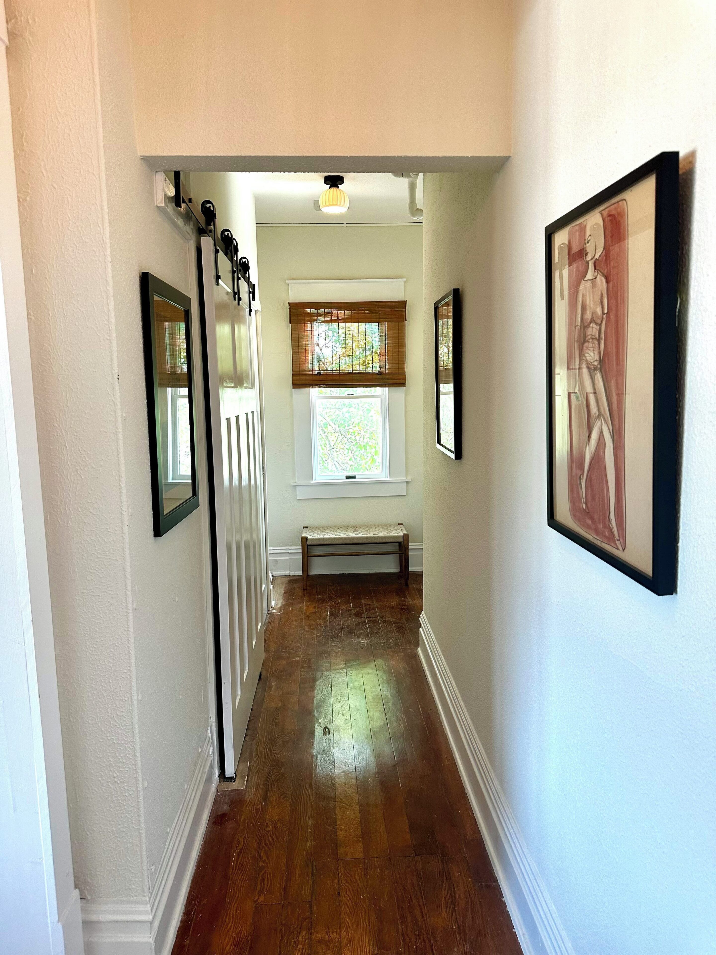 A hallway with wooden flooring, a bench, and framed artwork on the walls.