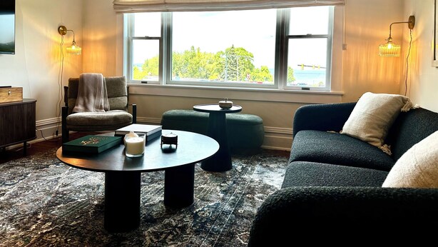 Un salon chaleureux avec une grande fenêtre, une table basse ronde, un canapé et un fauteuil.