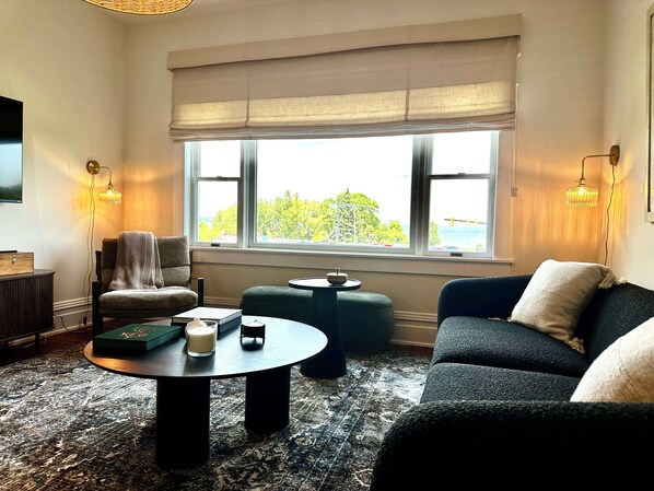 A cozy living room with a large window, a round coffee table, a sofa, and a chair.