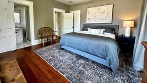 Une chambre à coucher avec un grand lit, une chaise en bois, une table de chevet et un luminaire au plafond.