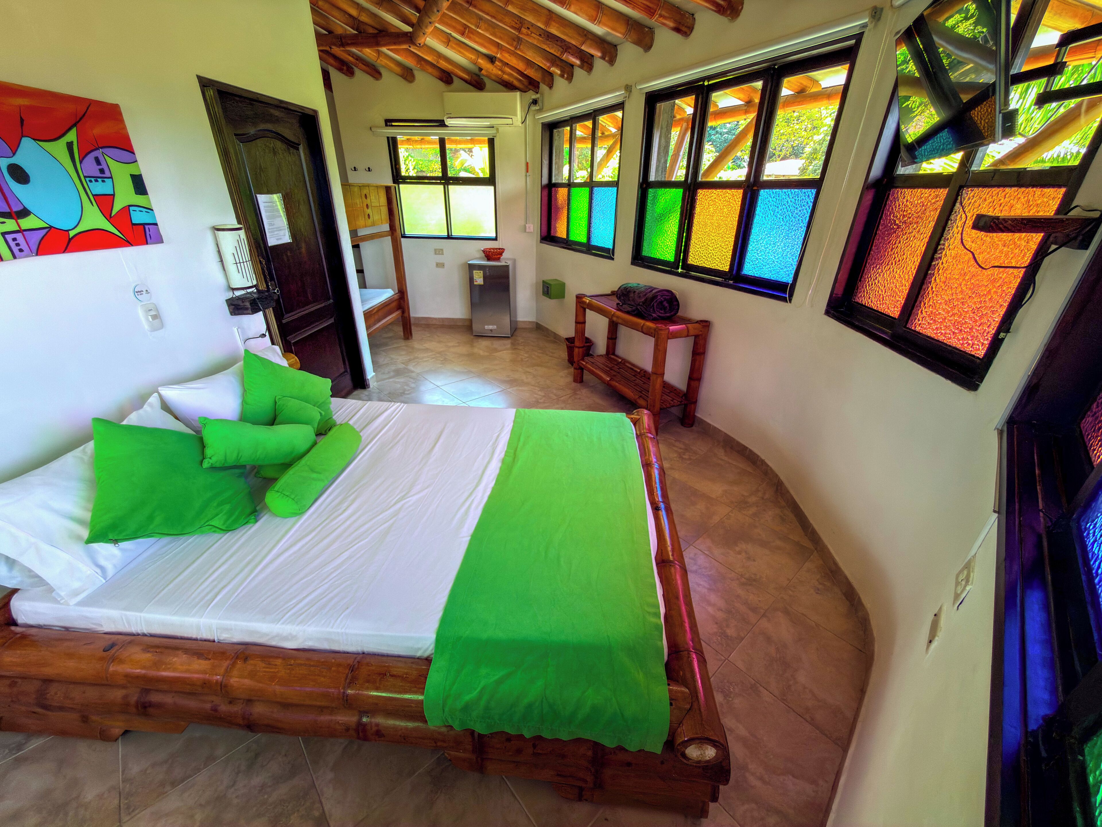A room with a bed, green pillows, a wooden headboard, a small table, and a colorful abstract painting on the wall.