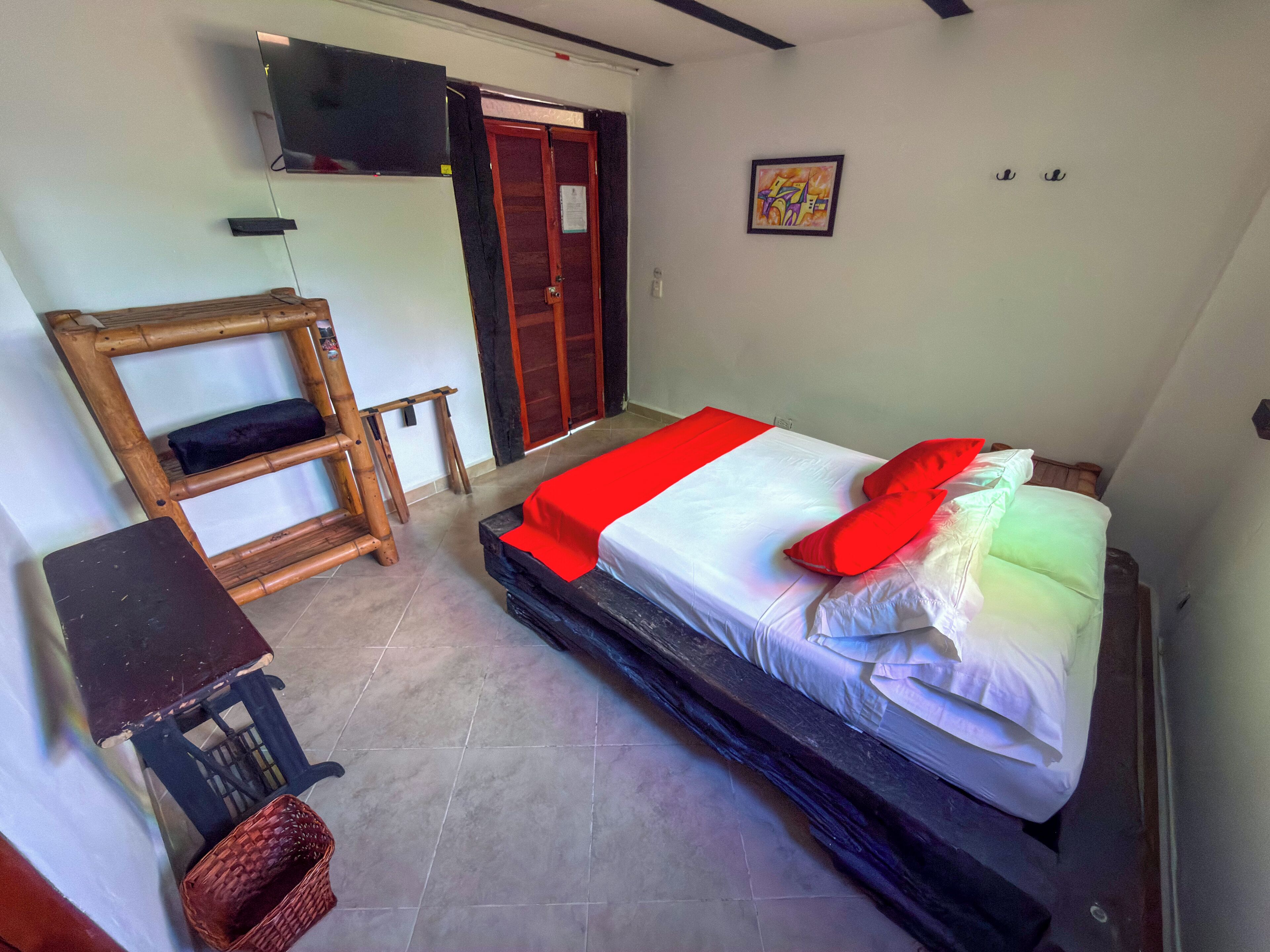 Una habitació amb un llit, escriptori, televisió penjada a la paret i una porta.
