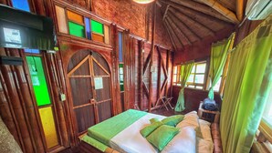 A rustic wooden room with a bed, a green curtain, and a window with green panes. - Solvae (San Jeronimo)