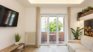 A modern living room with a flat-screen TV, a sofa, a coffee table, and a balcony with a view of buildings and trees. - Spacious BnB with 3 rooms and kitchen, a few steps from St. Peter's (Roma)