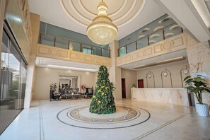 Eine geräumige Lobby mit einem zentral platzierten Weihnachtsbaum, einer prunkvollen Kandelaber und einem Marmorboden.