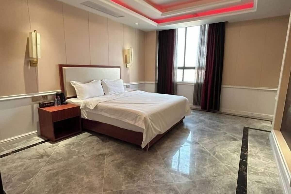A hotel room with a large bed, a nightstand, a wall-mounted lamp, and a window with curtains.