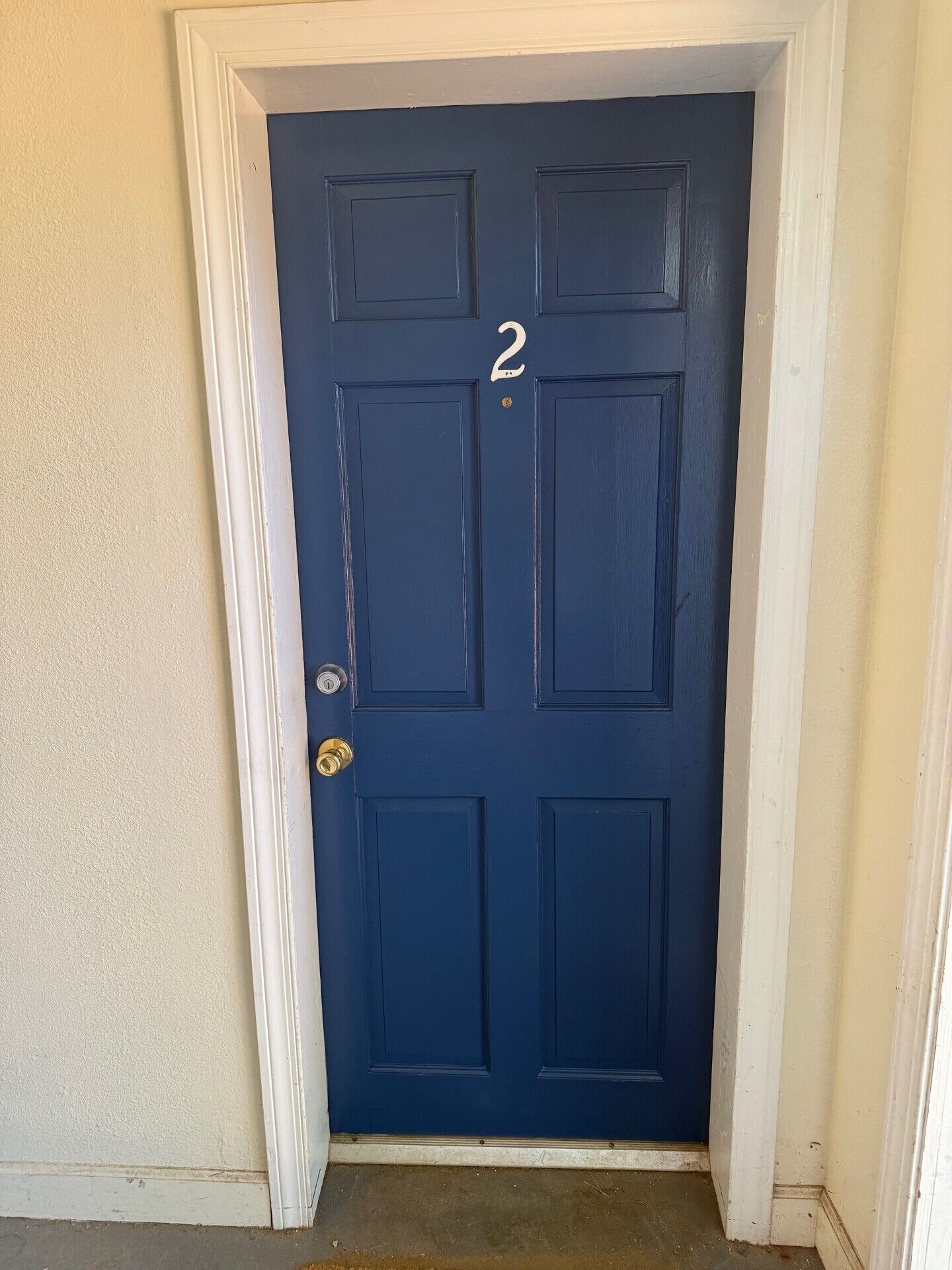 Une porte bleu foncé portant le numéro 2, avec des moulures blanches et un trou de serrure.