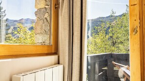 Une pièce avec une porte en bois, une fenêtre donnant sur un paysage verdoyant et des montagnes, et un radiateur.