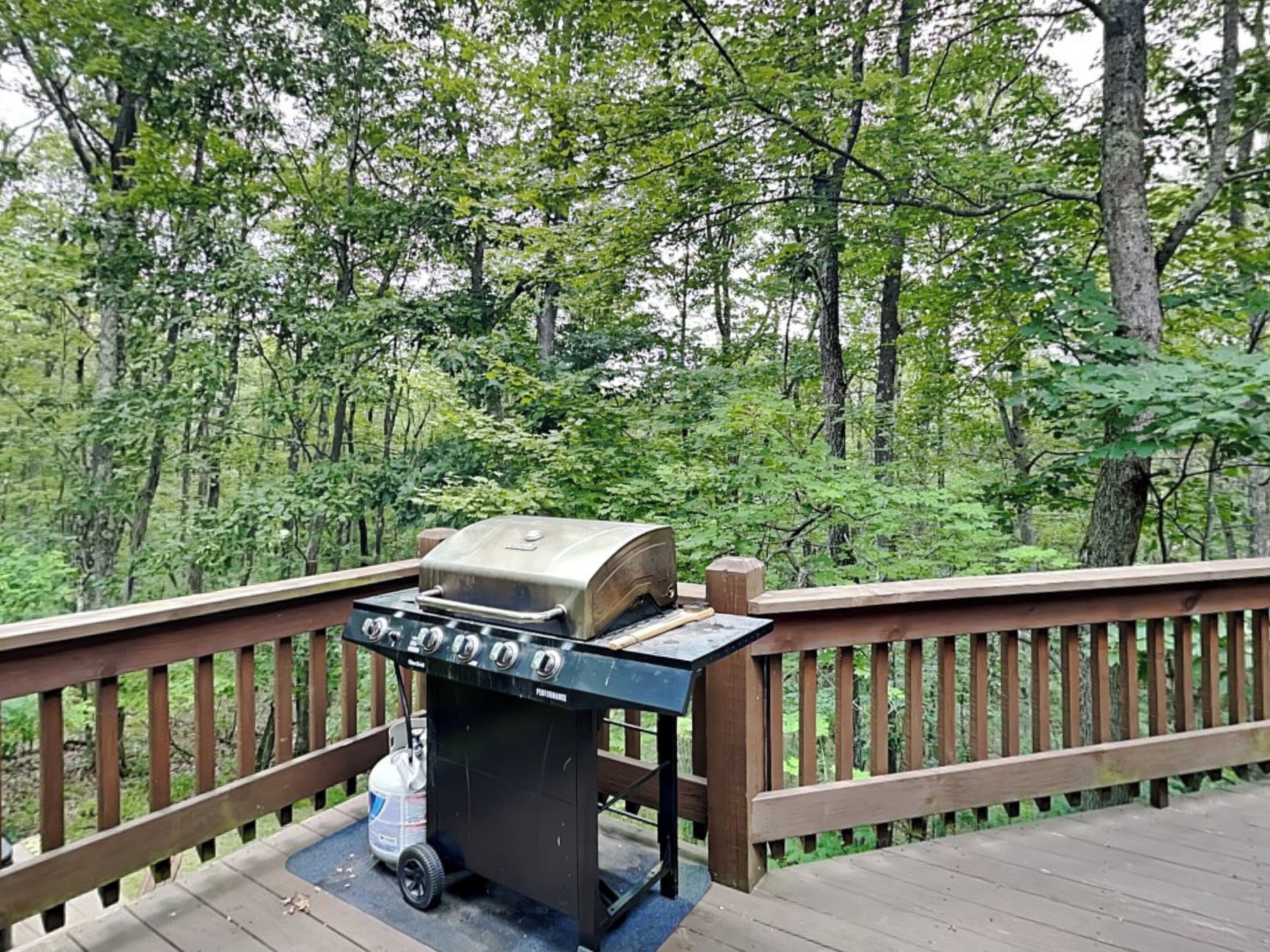 A portable grill on a wooden deck with a forest backdrop.