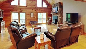 Un salon spacieux avec des murs en bois, une cheminée en pierre, un grand téléviseur et des canapés en cuir.