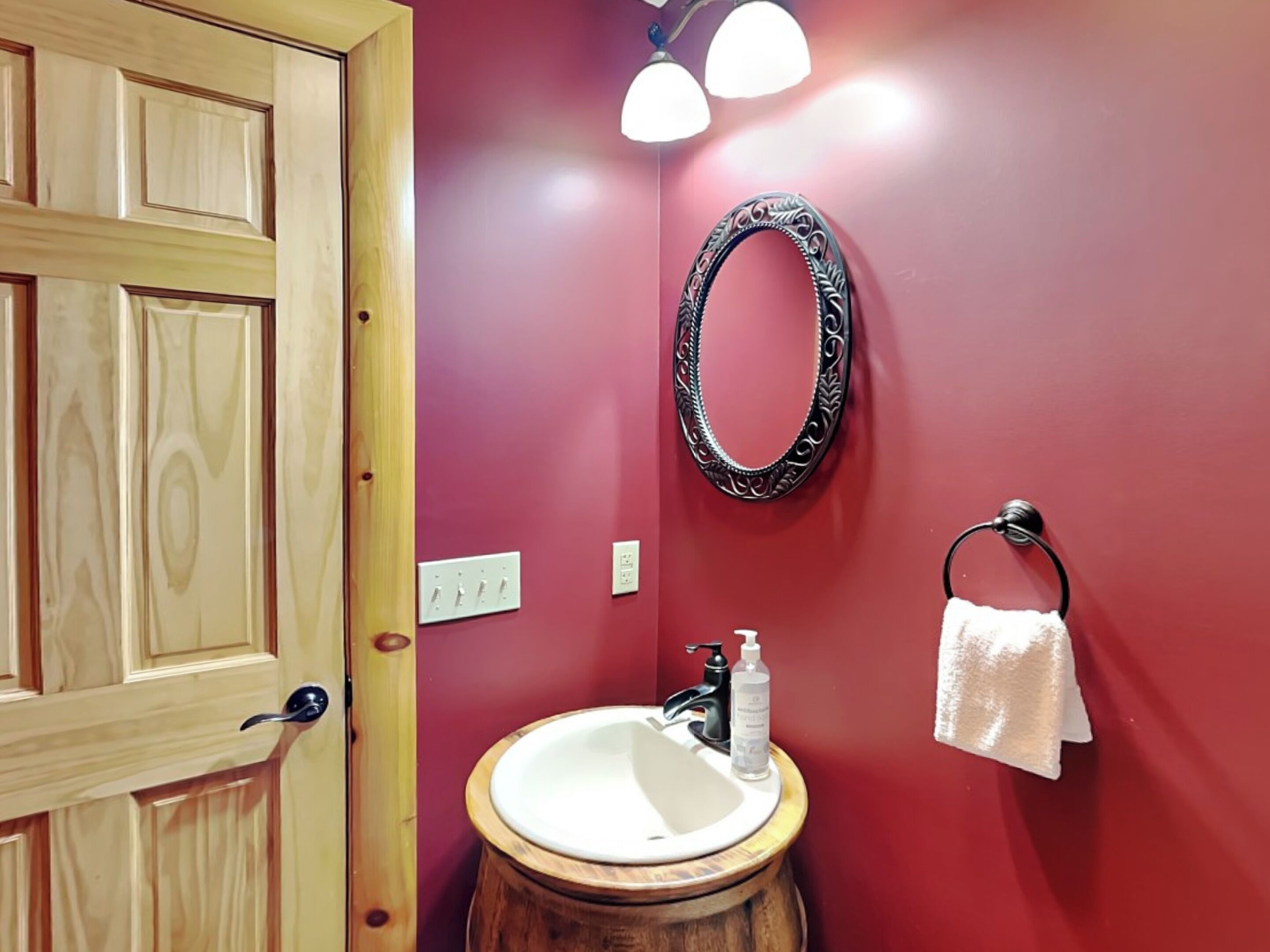 Une salle de bain avec une porte en bois, un lavabo blanc, un miroir et un porte-serviettes.