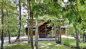 Une cabane entourée d’arbres, dotée d’un porche et d’une petite terrasse.