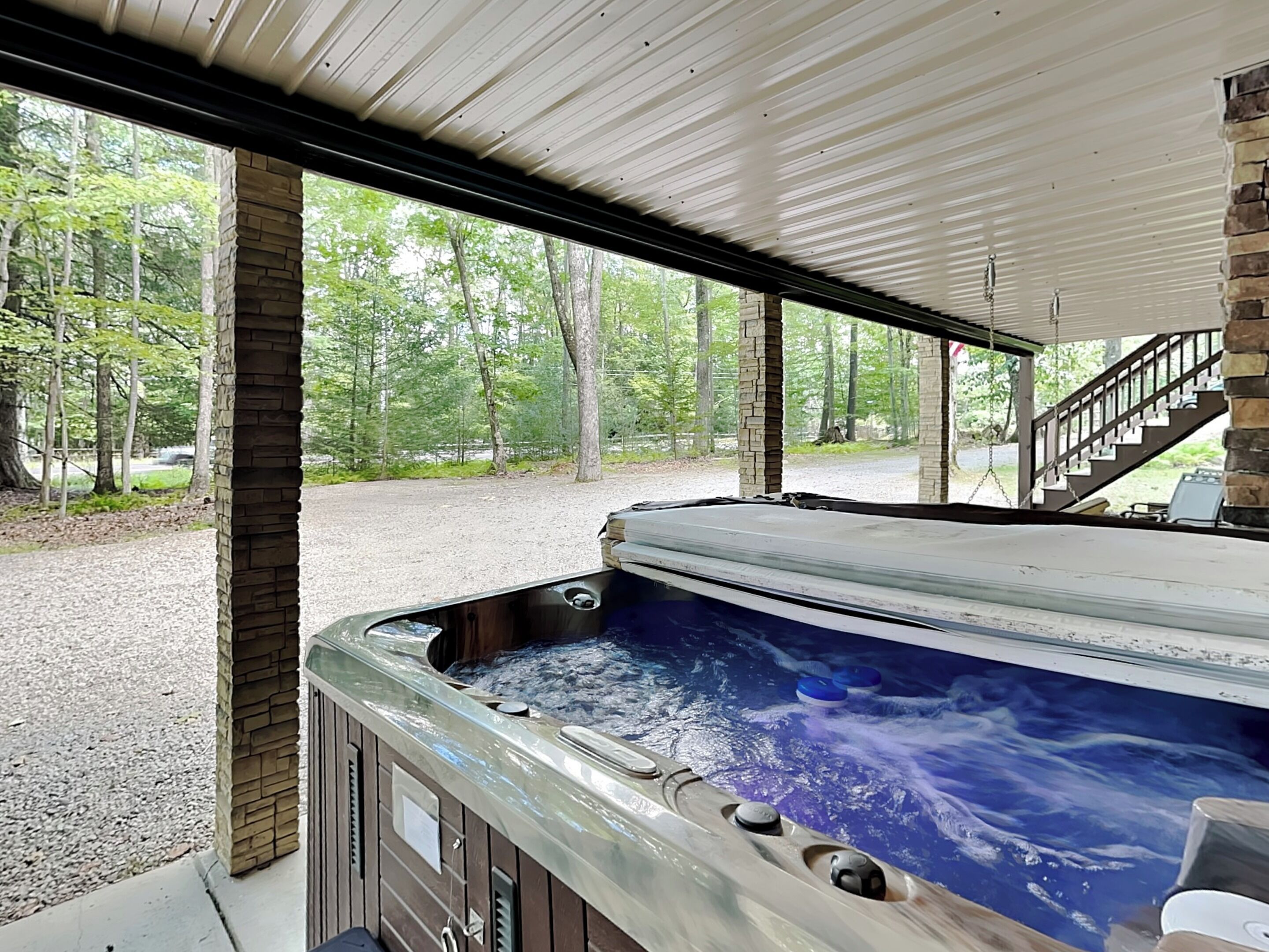 A hot tub with a stone exterior, set under a covered area with a view of a forested area.