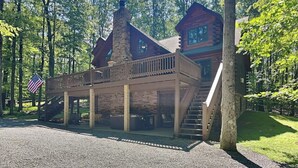 A cabin with a stone chimney, wooden deck, and a staircase leading to a second level. - Log Heaven by Taylor Made Deep Creek (Oakland)