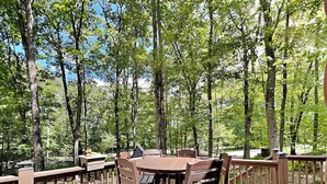 A wooden deck with a round table and chairs, surrounded by tall trees. - Log Heaven by Taylor Made Deep Creek (Oakland)