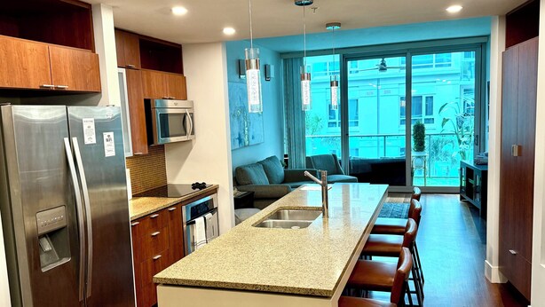 A modern kitchen with a central island, stainless steel appliances, and a view to the outside. - Luxury 2BR/2BA Channelside Condo- Pool, Sauna, Gym + Balcony (Tampa)