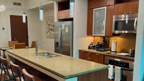 A modern kitchen with a granite countertop, stainless steel appliances, and a bar area with stools. - Luxury 2BR/2BA Channelside Condo- Pool, Sauna, Gym + Balcony (Tampa)