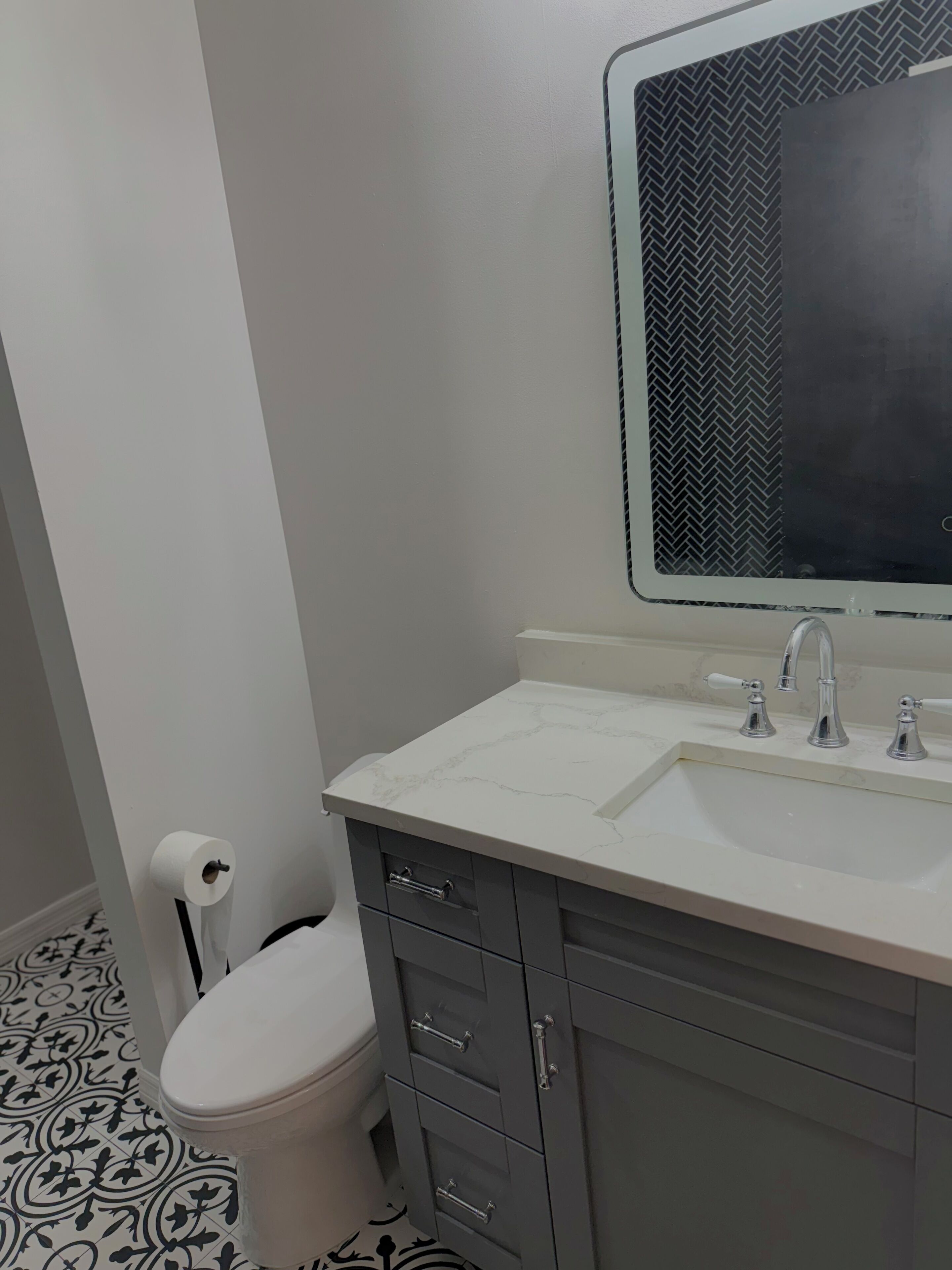 Un baño con inodoro, lavamanos con espejo y piso estampado.