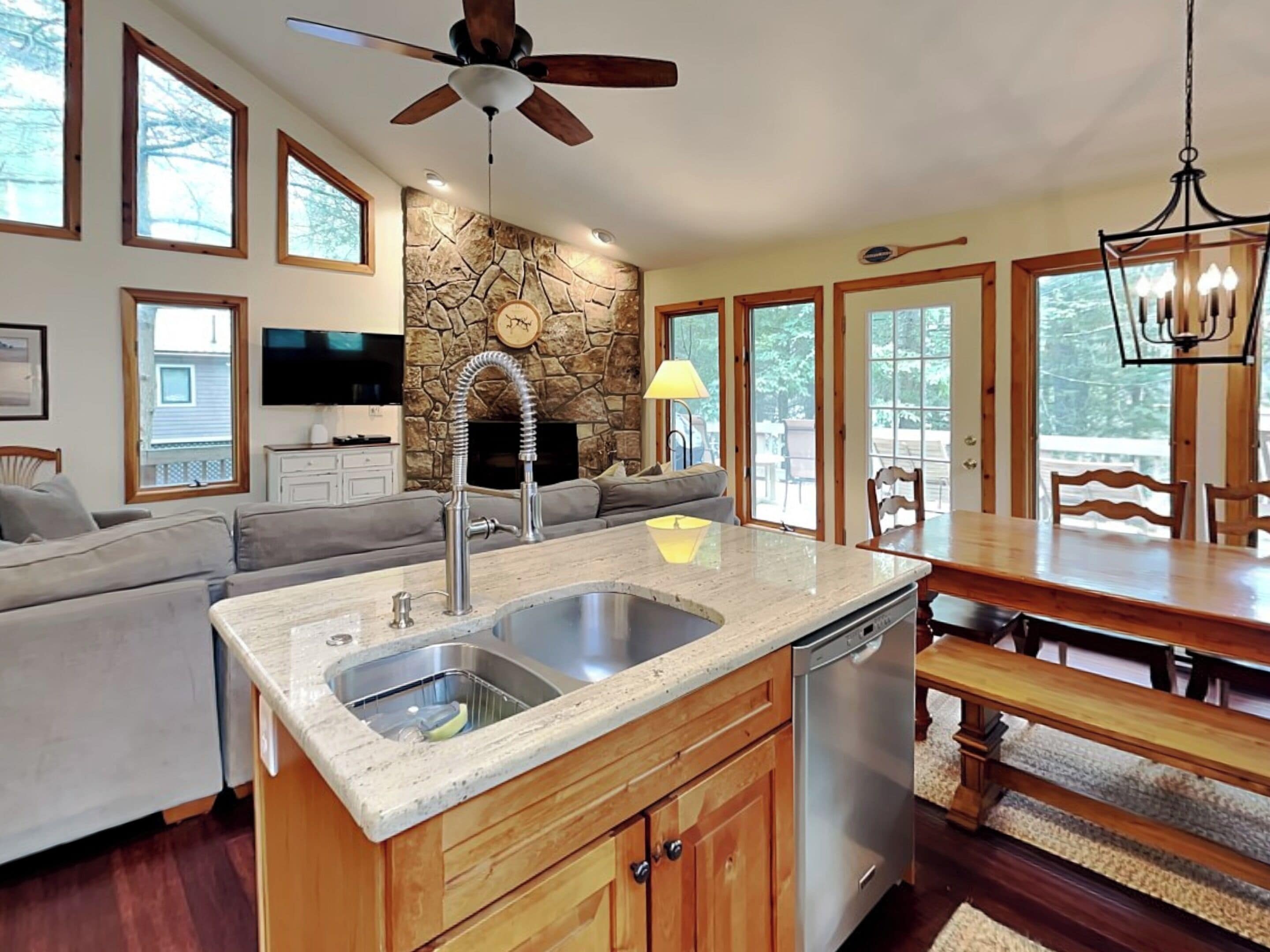 A modern kitchen with a stone backsplash, wooden cabinets, a built-in dishwasher, and a dining area with a wooden table and chairs.