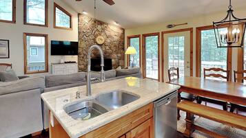 A modern kitchen with a stone backsplash, wooden cabinets, a built-in dishwasher, and a dining area with a wooden table and chairs.