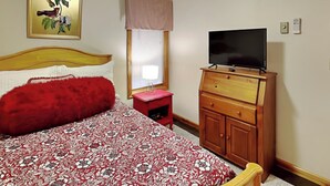 Una camera da letto con un letto, una televisione su una cassettiera in legno, una finestra con persiane e una ventola a soffitto.
