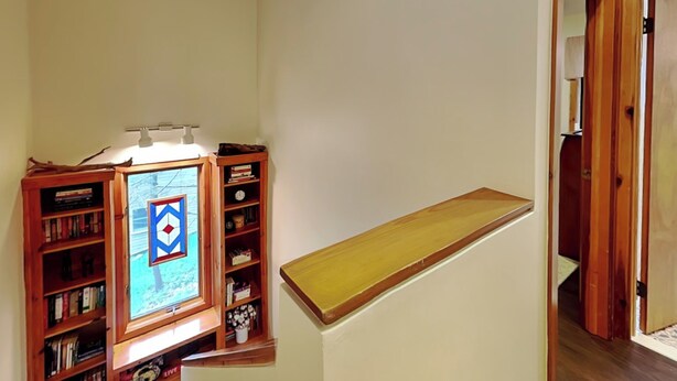 Una scala con ringhiera in legno, una libreria di legno piena di libri e un quadro appeso al muro.