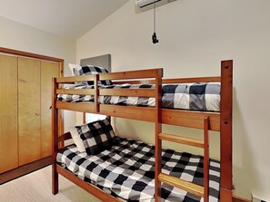 Egy emeletes ágy kockás ágytakaróval és párnákkal, egy fa szekrény, és egy mennyezeti ventilátor.
