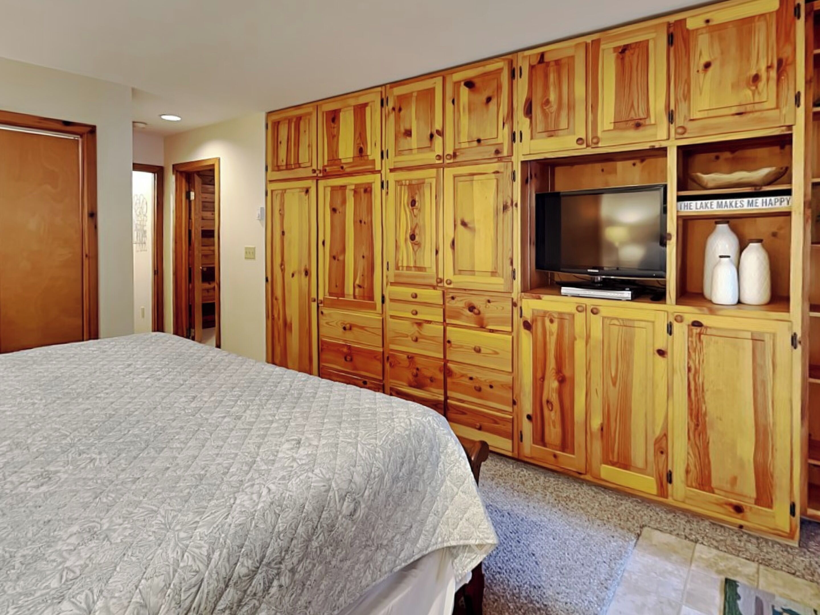 A bedroom with a large bed, wooden wardrobe, and a television.