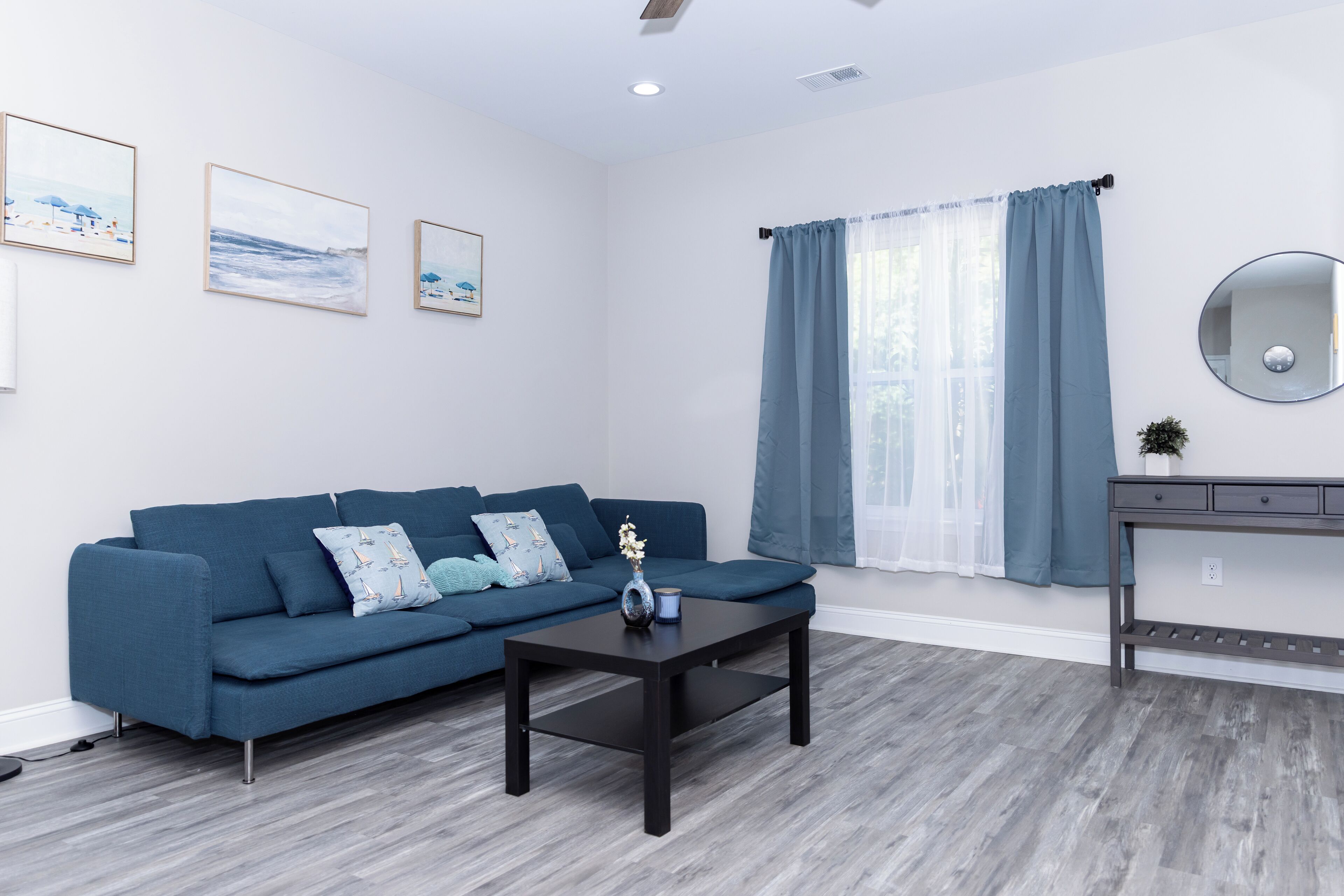 A modern living room with a dark blue sofa, a coffee table, and a large window with blue curtains.