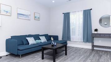 A modern living room with a dark blue sofa, a coffee table, and a large window with blue curtains.