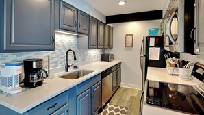 A modern kitchen with blue cabinets, a stainless steel sink, a coffee maker, and a refrigerator. - Arrowhead Village 13 by Taylor Made Deep Creek (Oakland)