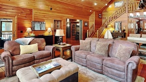 A cozy log cabin interior with a fireplace, plush seating, and a staircase leading to an upper level. - Crow's Point Lakehouse by Taylor Made Deep Creek (Swanton)