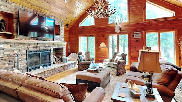 A cozy cabin interior with a stone fireplace, leather sofas, and a television. - Crow's Point Lakehouse by Taylor Made Deep Creek (Swanton)