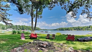A lakeside outdoor seating area with Adirondack chairs and a fire pit. - Crow's Point Lakehouse by Taylor Made Deep Creek (Swanton)
