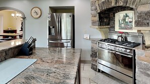 A kitchen with a granite countertop, stainless steel appliances, a stone fireplace, and a clock on the wall.