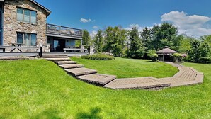 A stone building with a balcony, a paved pathway, and a gazebo in a grassy area.